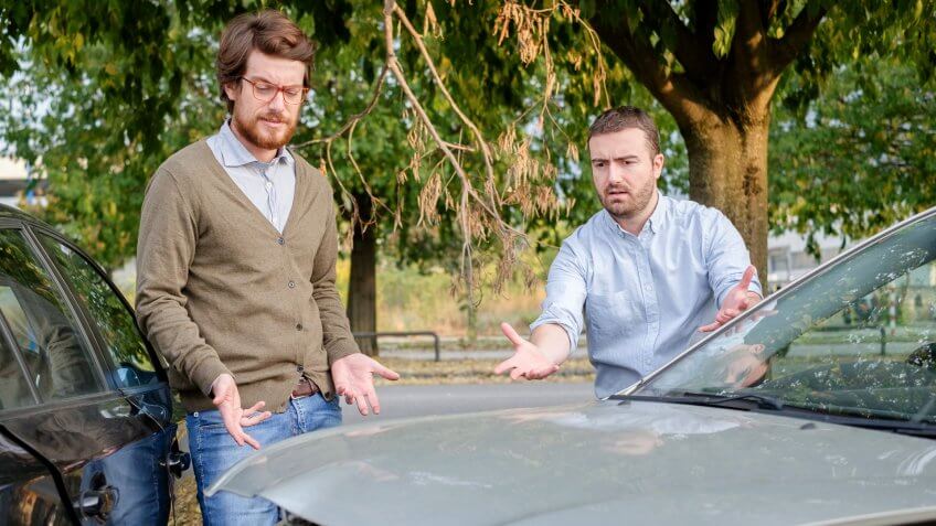 Two men arguing after a car accident on the road.