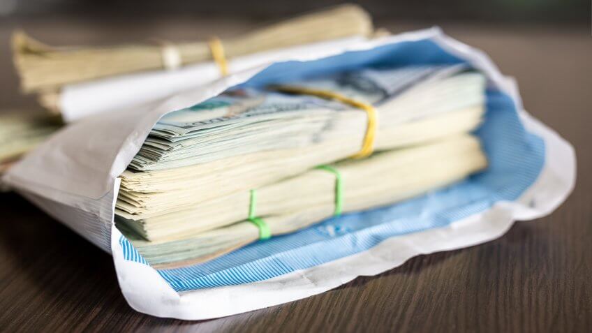 Bundle of american dollar banknotes in white envelope on wooden table.