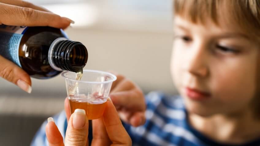 Close up of unrecognizable mother pouring cough syrup into a dose for her small boy at home.