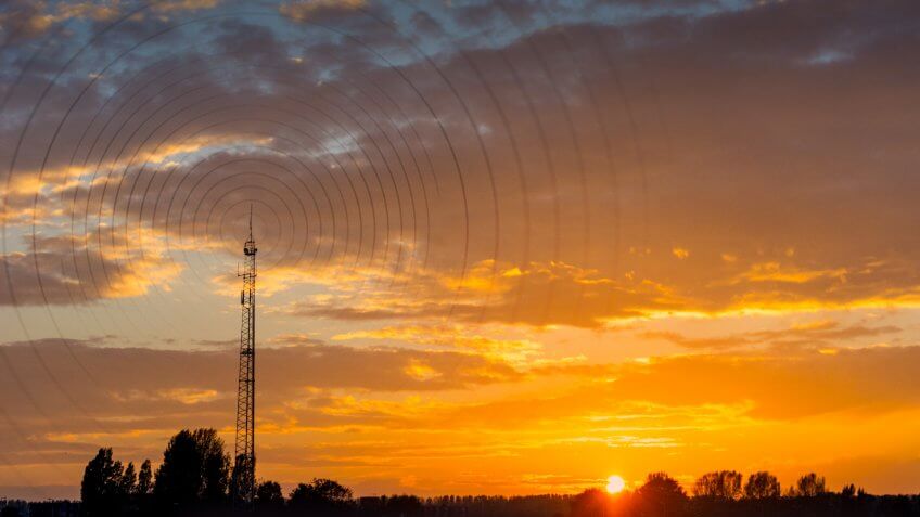 Radio waves escaping from gsm tower visualisation at sunset in rural area.