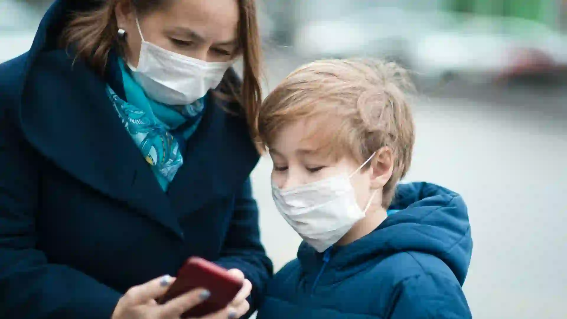 Child and his mother wearing facial mask on a city street.