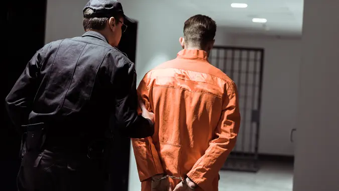 rear view of prison officer leading prisoner in handcuffs in corridor.