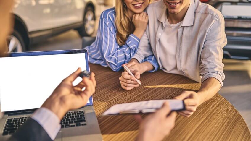 Happy young couple buyers signing a contract of buying a new car.