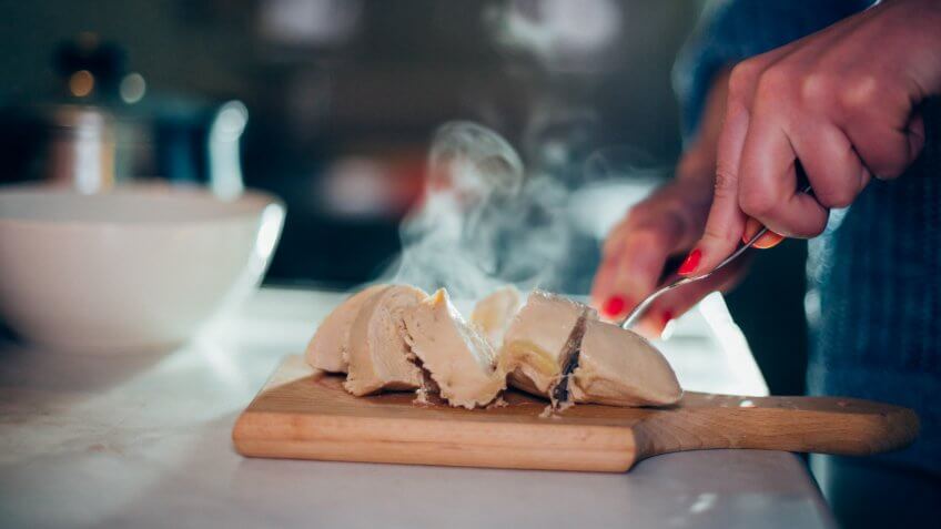 Close-up of a woman cutting chicken breasts on the kitchen counter.