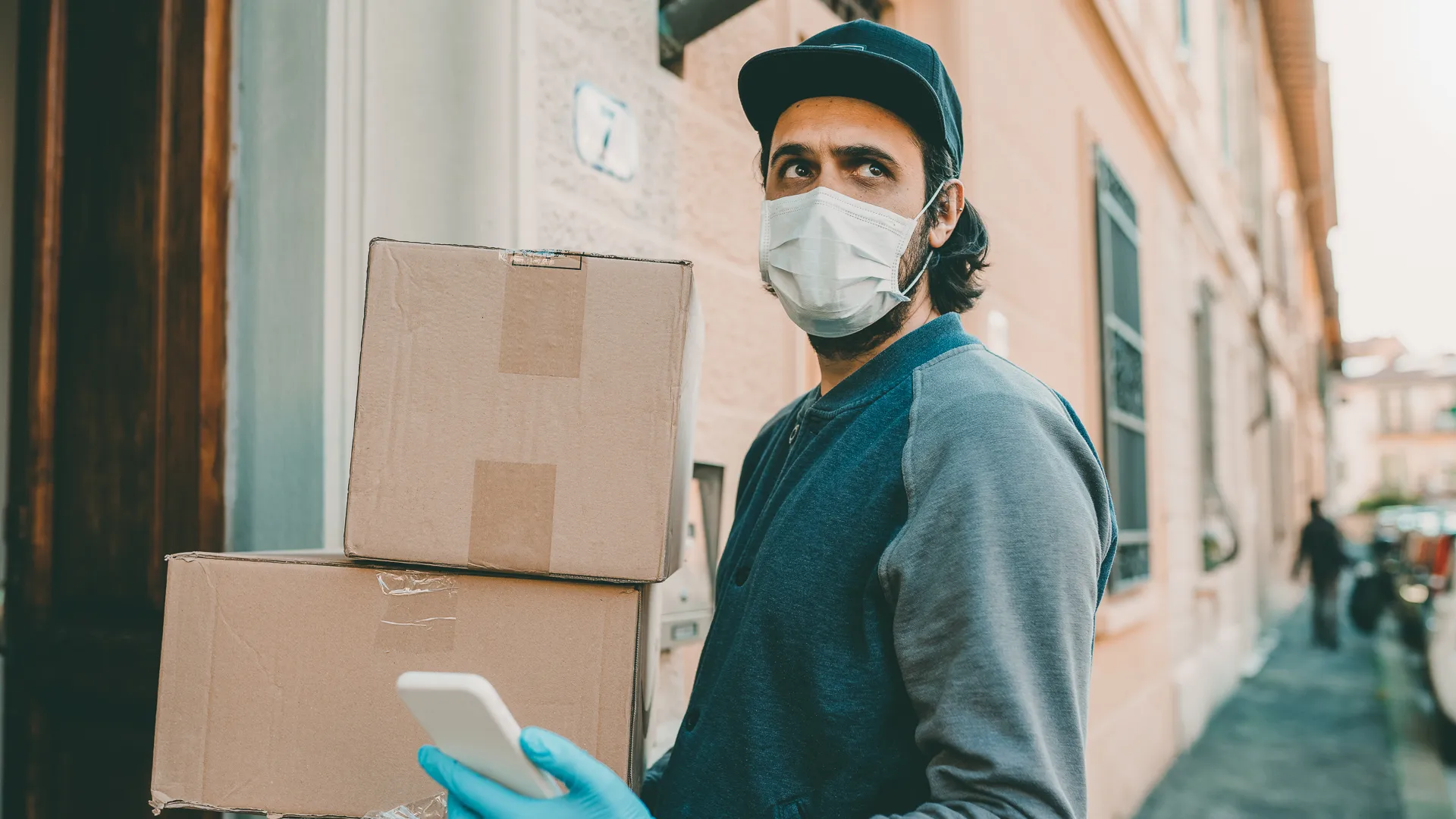 Delivery man is checking his smart phone near the entrance door of a home.