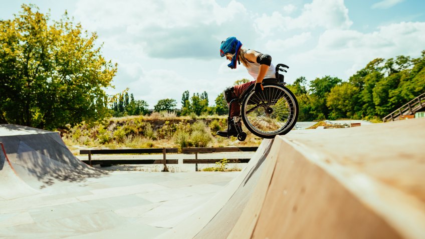 Wheelchair woman performing stunts in skate park - courage and confidence in adaptive sports and hobbies.