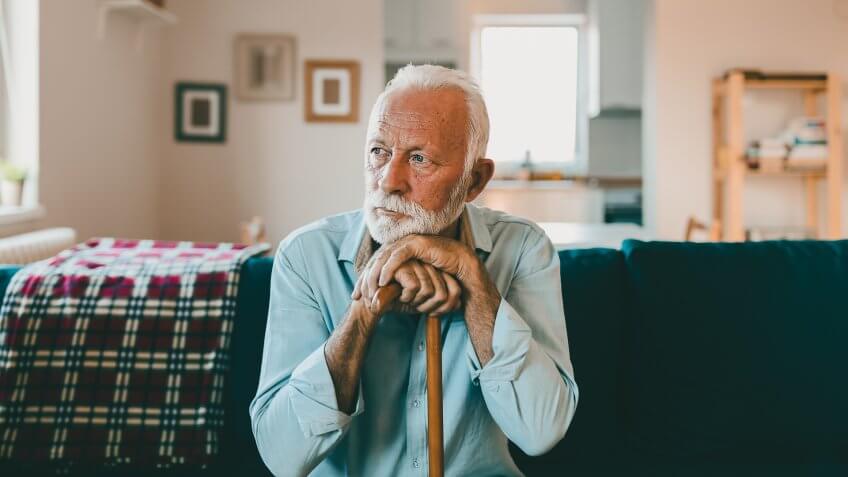 Hands of a thoughtful old man leaning on a cane, sitting at home.