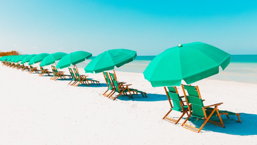 Green beach loungers and umbrellas at white sandy beach.
