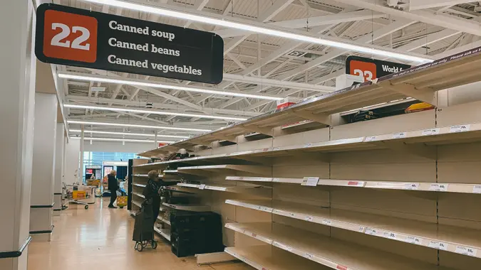 People shopping mostly empty shelves at a grocery store due to panic buying.