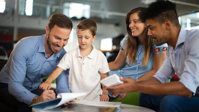 Car salesman hands over the car keys to a family man signing papers in a car dealership showroom.