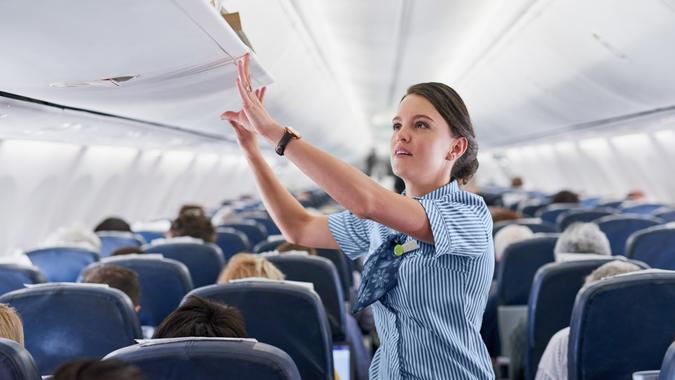 Shot of a young air hostess closing the overhead compartment on an airplane.