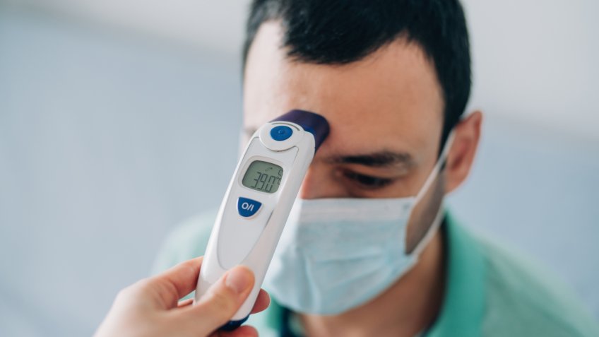Healthcare worker checking body temperature of a young sick man with contactless digital infrared thermometer.
