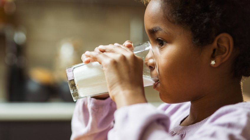 Little African American girl drinking fresh milk from glass at home.