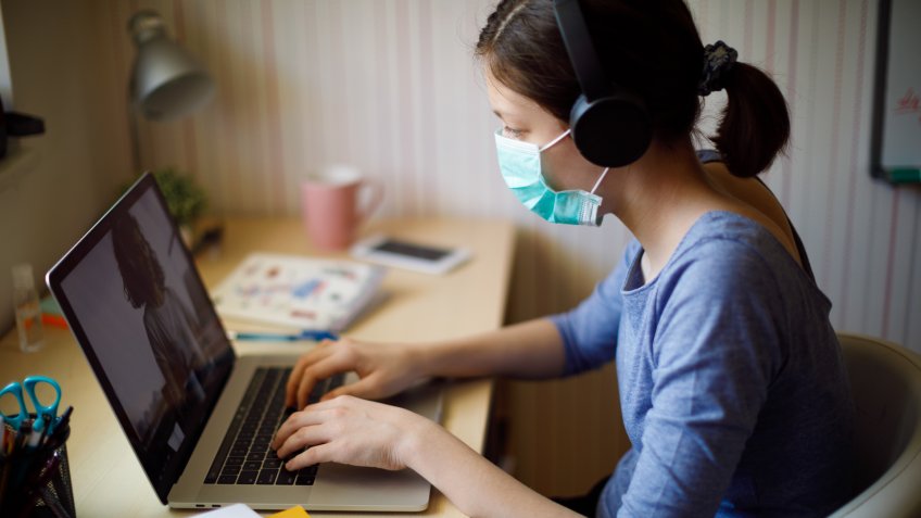 Teenage girl with face protective mask having online school class at home.