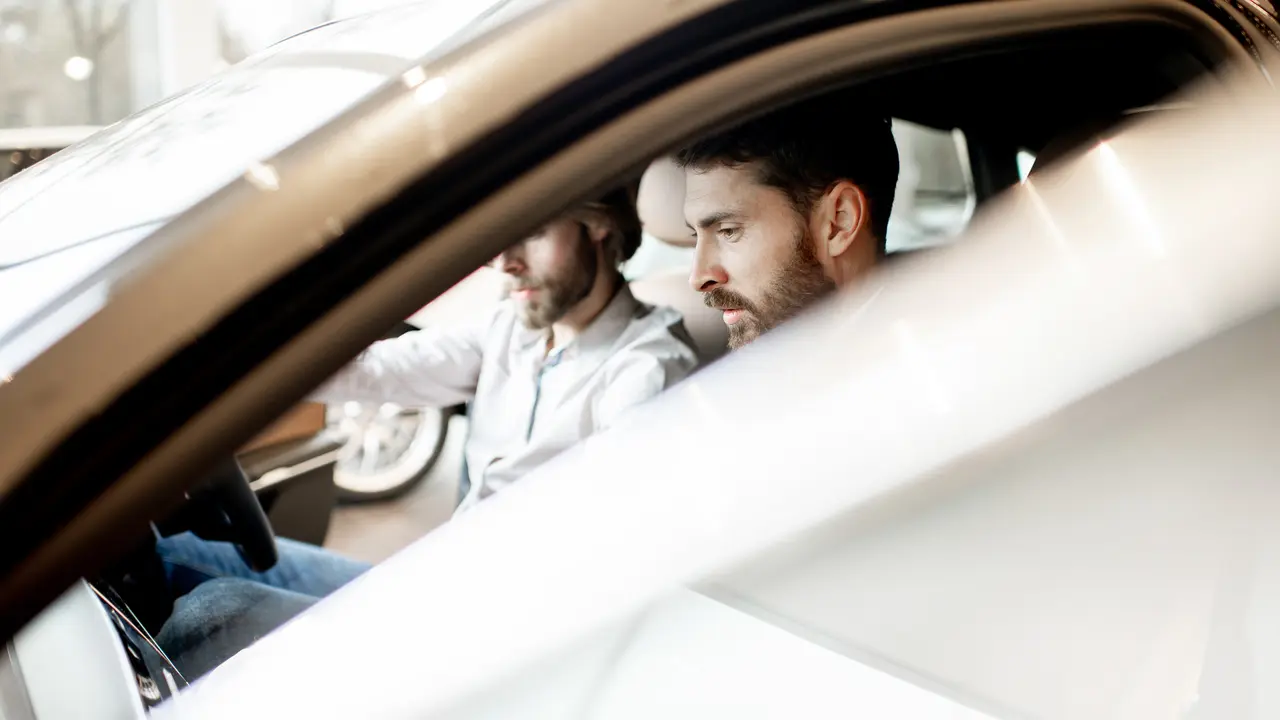 Young man trying new car sitting with salesperson in the luxury car interior at the showroom.