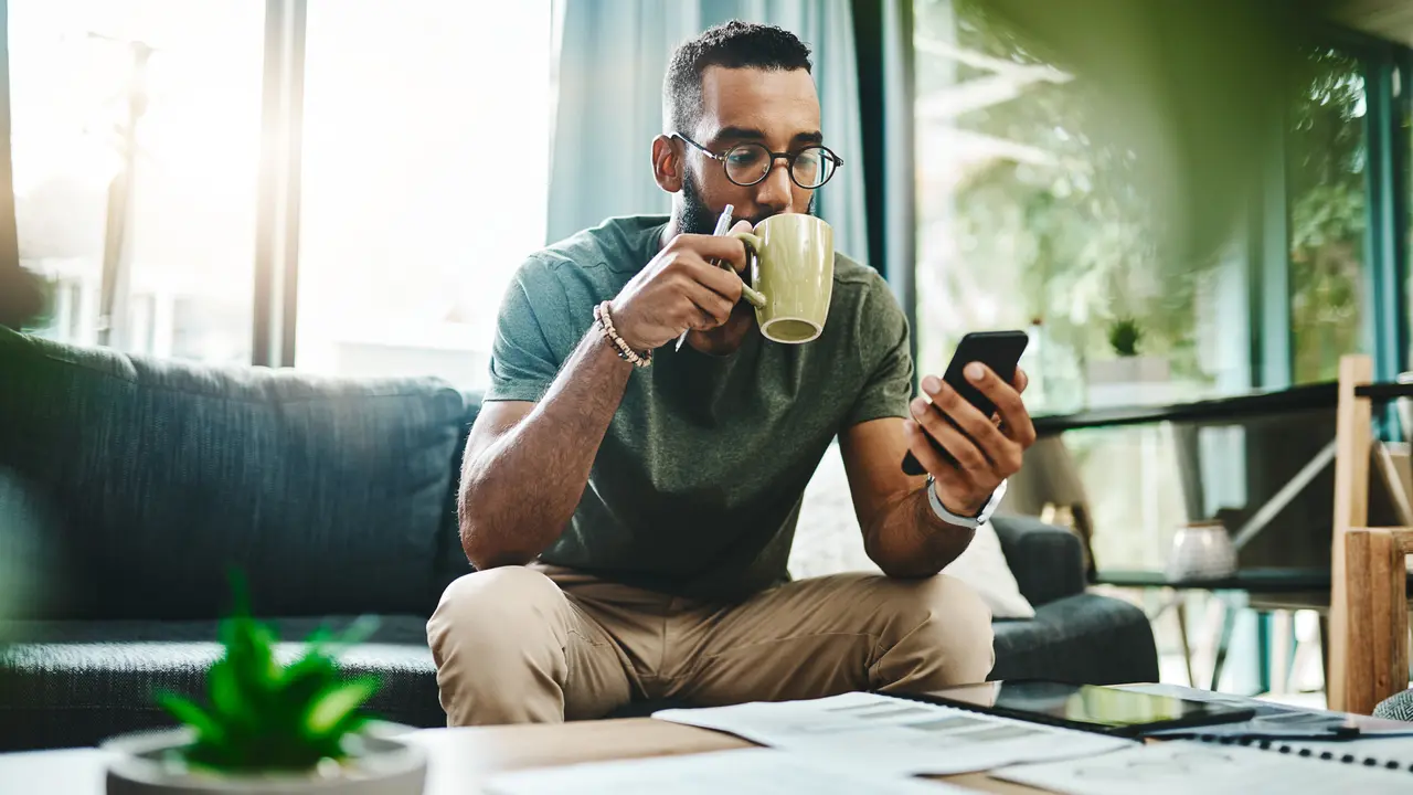 Shot of a Young Man sitting on a couch using a smartphone while going over his finances at home.