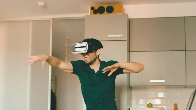 Funny young man in virtual reality 360 headset dancing in the kitchen in the morning while listening to music and have fun at home.