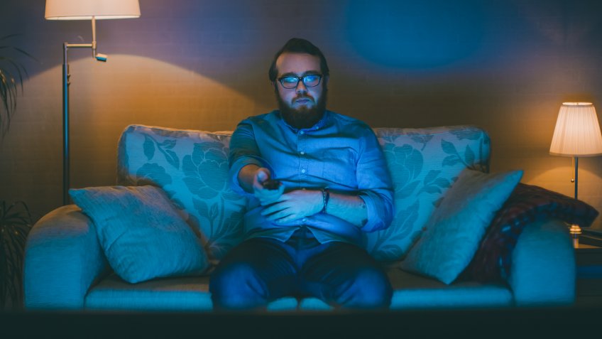 Portrait Shot of a Man Sitting on a Sofa in His Living Room, Watching TV, Changing Channels.