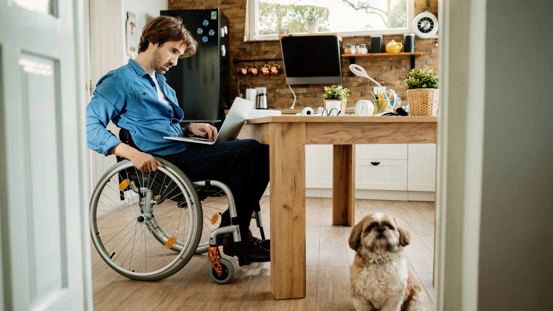 年轻的残疾人自由工人工作在电脑上,带着他的狗在家里。
