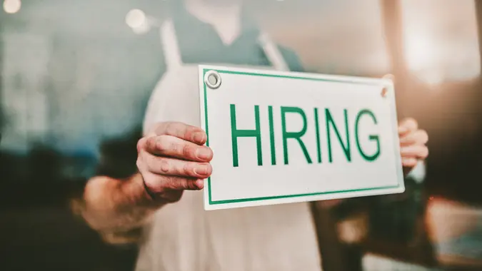 Cropped shot of an unrecognizable male coffee shop owner hanging a "HIRING" sign in his window.