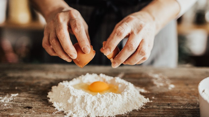 Woman adds an egg to the flour.