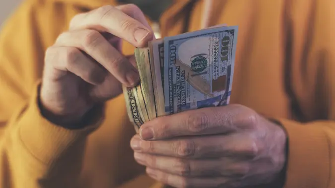 Casual man is counting american dollar banknotes, close up of hands with money.