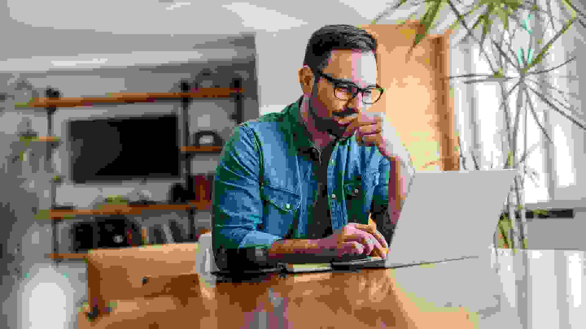 Pensive man looking at laptop while sitting at wooden table, portrait.