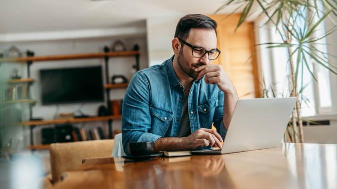 Pensive man looking at laptop while sitting at wooden table, portrait.