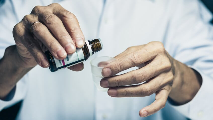 old woman hands close up holding medicine bottle and puts drops in a glass, healthcare concept background with copy space.