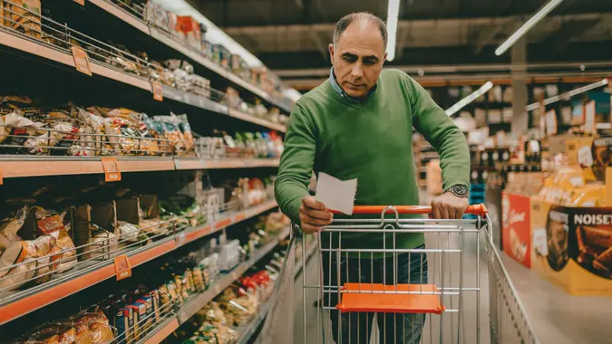 Mature man with a shopping list buying groceries in the supermarket.