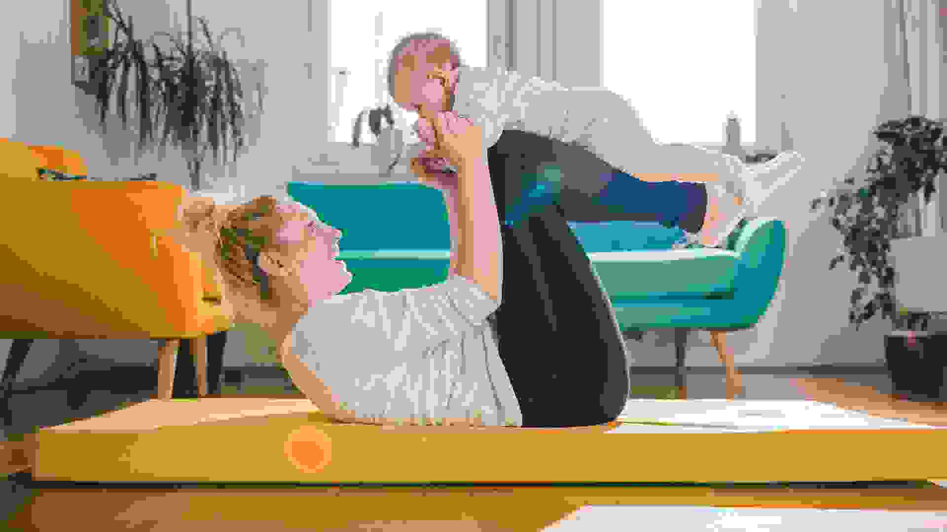 Mother Exercise With Her Baby on yellow mat At Home.