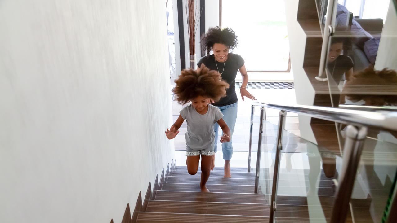 Excited little African American girl run up stairs of new home with young mom, happy black mother and small daughter explore bought house on moving day together, mommy have fun playing with kid.