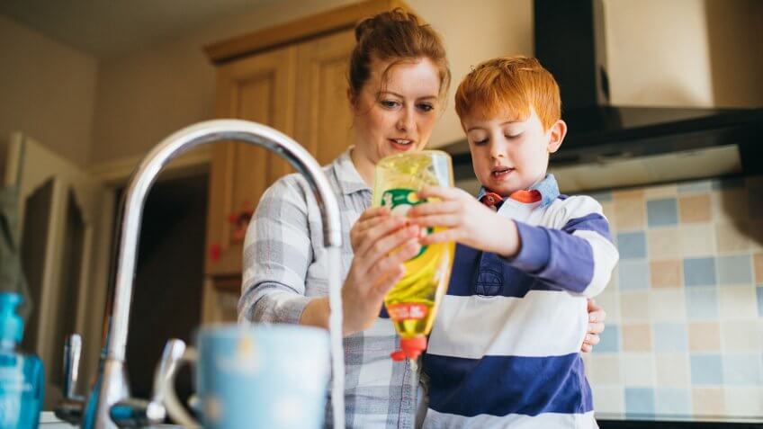 Little boy and his Mother washing the dishes in the kitchen sink.