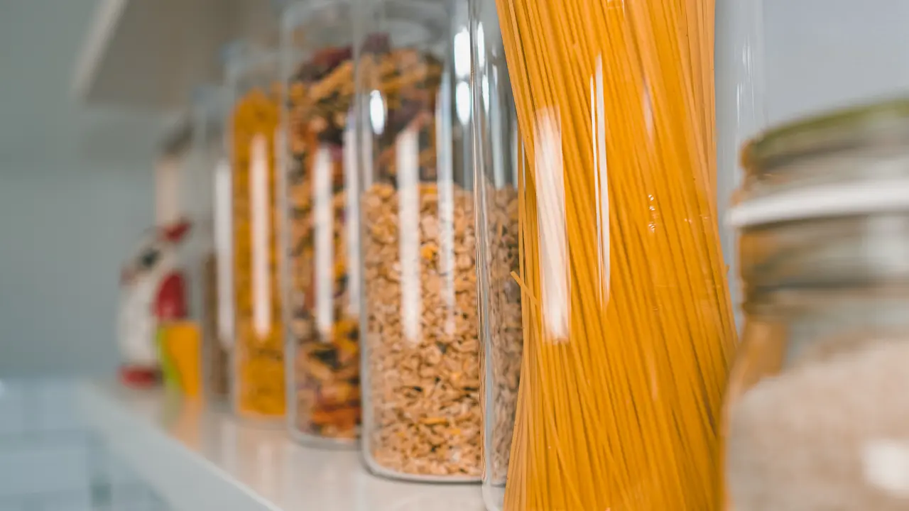 Various uncooked groceries in glass jars arranged on wooden white shelves ar the kitchen.