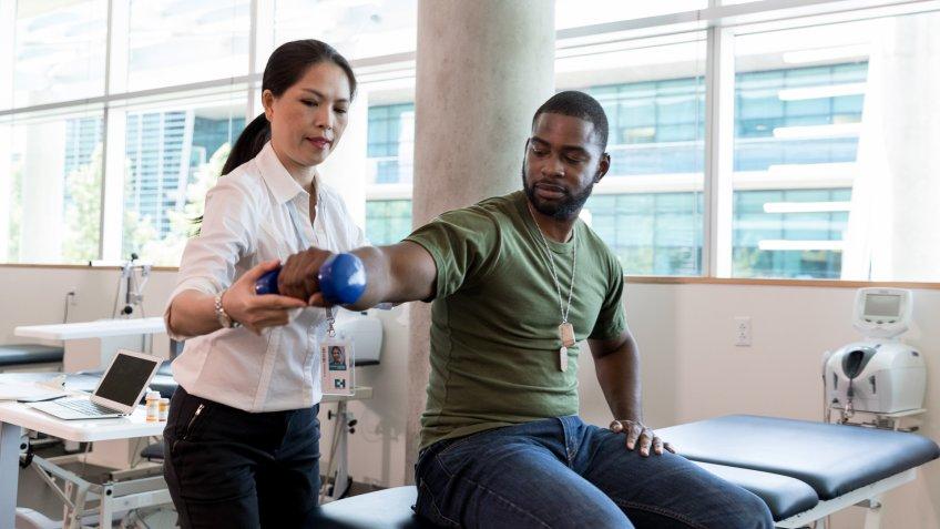 Serious army soldier with injury uses a hand weight during a physical therapy session.