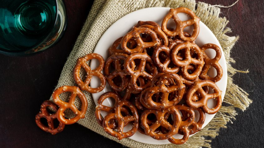 Macro photograph of pretzels on white plate on dark red black background.