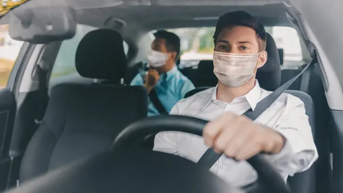 health protection, safety and pandemic concept - male taxi driver wearing face protective medical mask driving car with passenger.