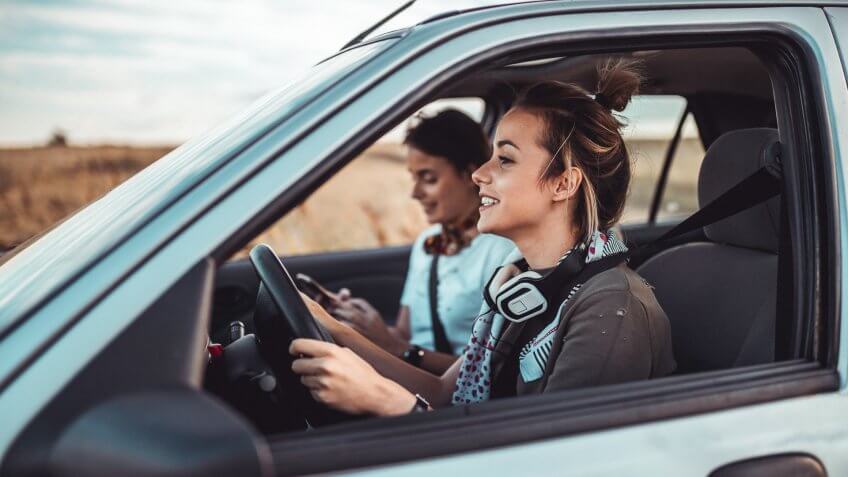 Beautiful twin sisters driving a car and enjoying summer road trip.