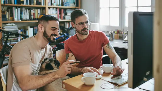 Gay couple with pug shopping through computer at desk.