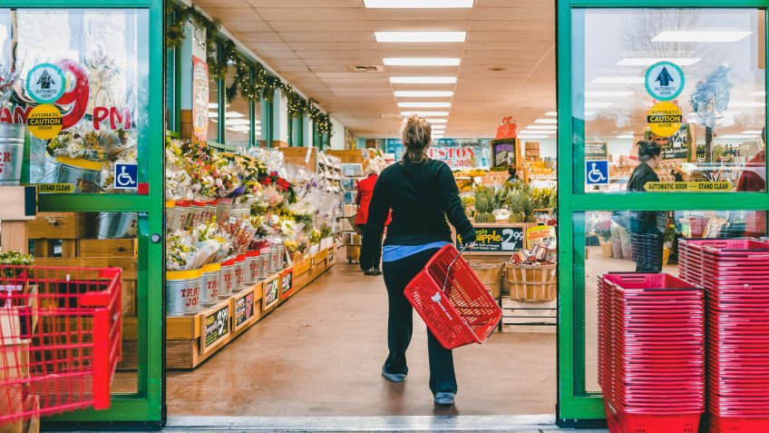 Reston, USA - December 18, 2017: Trader Joe's customer trolley shopping basket carrying carts by store entrance doors outside women, winter flower pots, gardening plants, pineapple in Virginia.