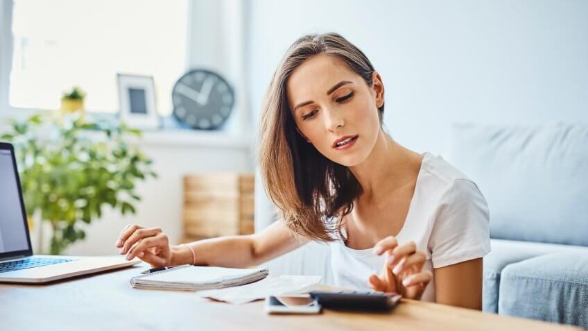 Young woman preparing home budget, using laptop and calculator.