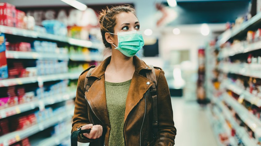 Young woman with face mask walking through grocery store during COVID-19 pandemic.