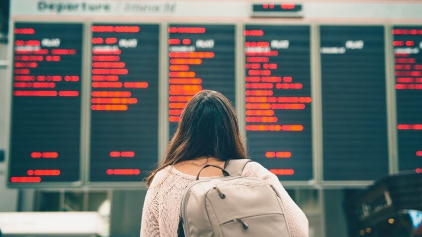 Rearview shot of an unrecognizable young woman looking at an arrivals and departures board while standing in an airport.