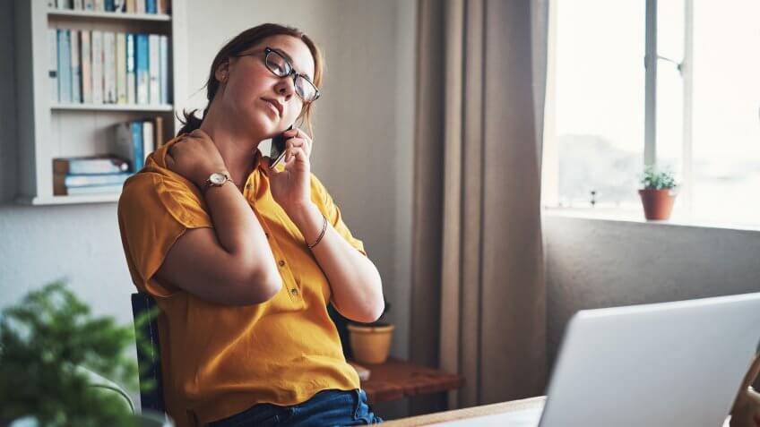 Cropped shot of an attractive young businesswoman sitting alone in her home office and feeling stressed while using her cellphone.