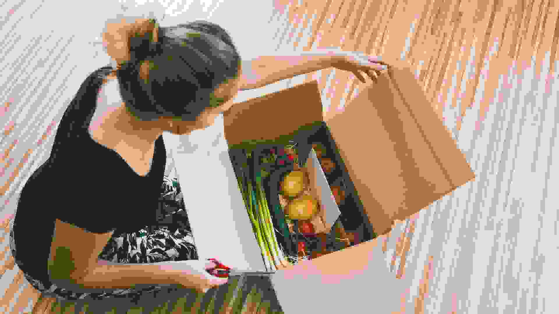 woman opening a vegetable delivery box at home, online ordering.