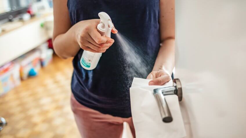 Woman cleaning a door handle with a disinfection spray and disposable wipe.