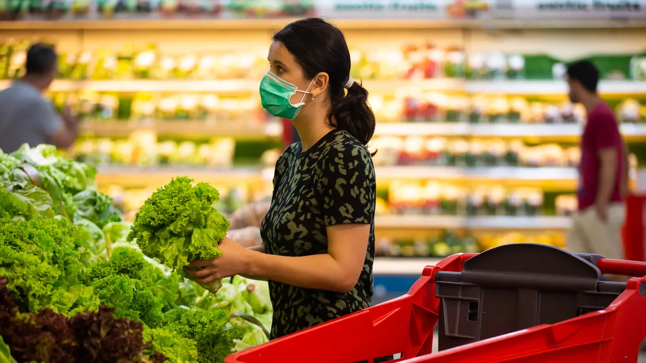 Alarmed female wears medical mask against coronavirus while grocery shopping in supermarket or store- health, safety and pandemic concept - young woman wearing protective medical mask for protection from virus covid-19 and stockpiling food.
