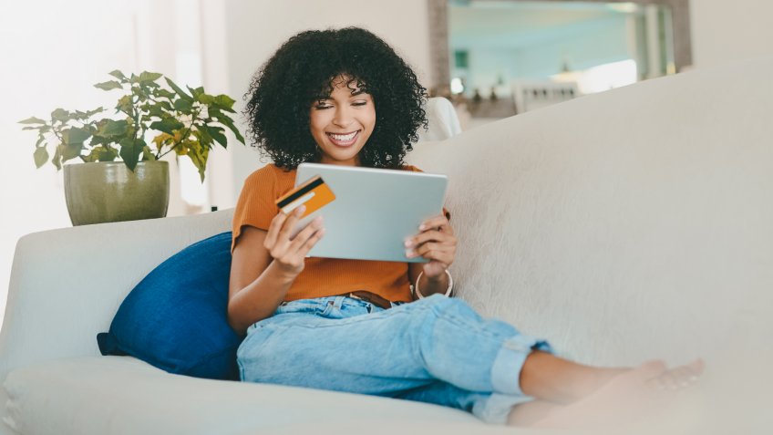 Shot of a young woman using a digital tablet and credit card while relaxing at home.