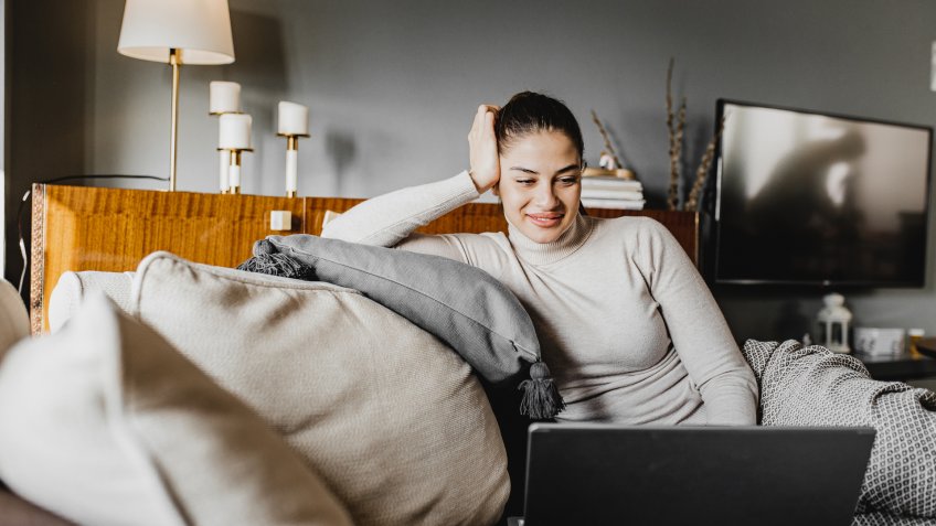 A young woman is at home and she is using a laptop and working remotely.