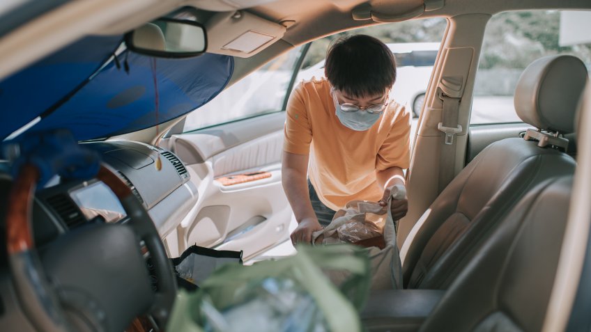 an asian chinese mid age woman removing reusable bags from her car which she just bought all groceries from supermarket with her face mask.